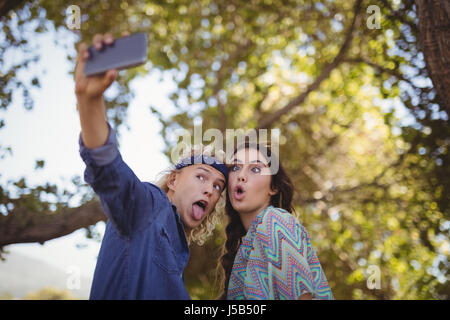 Glückliches Paar Grimassen während der Einnahme von Selfie gegen Bäume im Wald Stockfoto