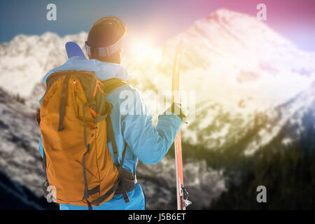 Rückansicht des Skifahrers mit Ski Rucksack gegen die malerische Aussicht auf die schneebedeckten Berge Stockfoto