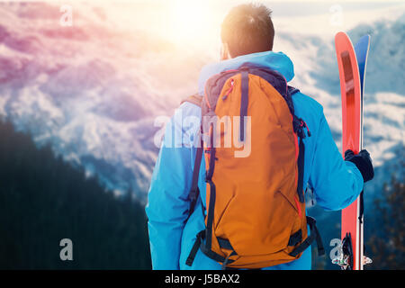 Rückansicht des Skifahrers mit Rucksack Ski an malerischen Blick auf Wald und verschneiten Gebirge halten Stockfoto