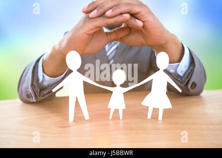 Hand zum Schutz einer Familie in Papier gegen Wiese unter einem sonnigen Himmel Stockfoto