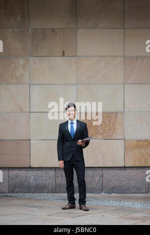 Voller Länge Portrait von einem chinesischen Geschäftsmann vor modernen Bürogebäude. Asiatische Geschäftsmann lächelnd & in die Kamera schaut. Stockfoto