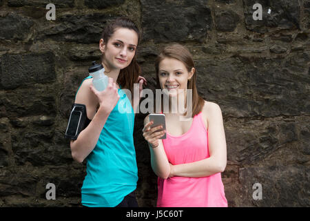 Zwei Läuferinnen, Austausch von Informationen über dort Smartphone nach gehen für einen Lauf.  Aktion und gesunden Lifestyle-Konzept. Stockfoto