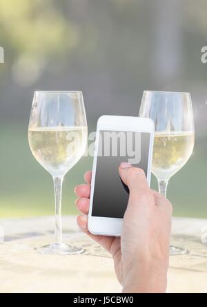 Digitalen Verbund von Hand Holding Telefon mit zwei Gläser Champagner und sonnigen grün Stockfoto