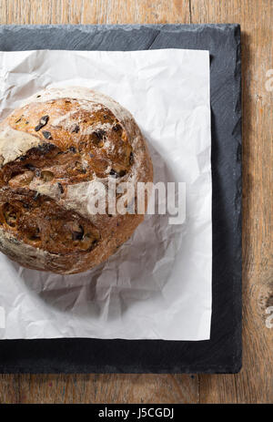 Runder Brotlaib auf schwarzen Schiefer Brett auf einem rustikalen Holztisch. Stockfoto