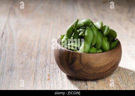 Schüssel mit Edamame sitzt auf einem rustikalen Holztisch. Stockfoto