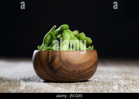 Schüssel mit Edamame sitzt auf einem rustikalen Holztisch. Stockfoto