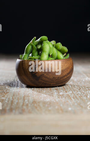 Schüssel mit Edamame sitzt auf einem rustikalen Holztisch. Stockfoto