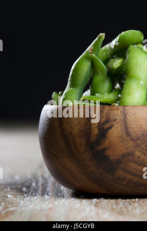 Schüssel mit Edamame sitzt auf einem rustikalen Holztisch. Stockfoto