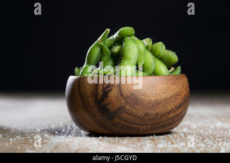 Schüssel mit Edamame sitzt auf einem rustikalen Holztisch. Stockfoto