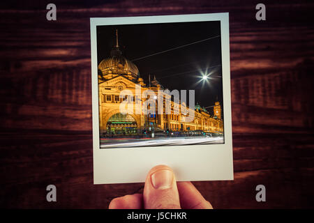Hand, die Polaroid-Postkarte der Flinders Street Station in der Nacht. Melbourne, Australien. Reisen Sie, Scrapbooking Erinnerungen an schöne Zeiten mit Textfreiraum Stockfoto