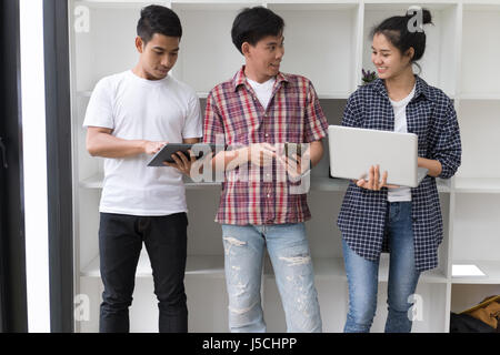 junge Asiaten sind mit verschiedenen Gadgets und lächelnd, stehen in der Nähe von weißen Wand. Männliche und weibliche Studenten tablet mit Laptop-Computer, Stockfoto