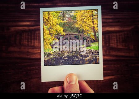 Hand, die Polaroid-Foto Herbst Szene im australischen Garten - schöne Holzbrücke über den Creek mit Textfreiraum. Erinnerungen an die guten alten Reisen Stockfoto