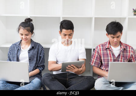 junge Asiaten sind mit verschiedenen Gadgets und lächelnd, sitzen in der Nähe von weißen Wand. Männliche und weibliche Studenten tablet mit Laptop-Computer. Stockfoto