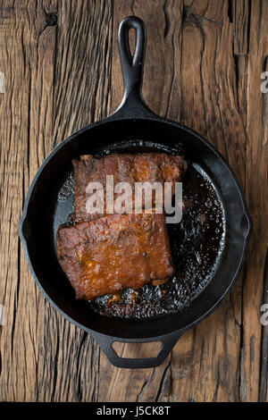 Geröstete Schweinerippchen in Scampispieß Soße auf einem rustikalen Holztisch sitzend. Stockfoto