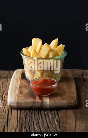In eine Glasschüssel serviert frische Pommes frites oder heiße Kartoffel-Chips. Das Essen ist auf einem rustikalen hölzernen Hintergrund sitzen. Stockfoto
