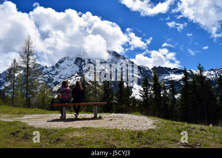 Zwei Frauen sitzen auf Bank und beobachten schönen Blick auf die Berge der Alpen. Ort: Rossfeldstrasse Panoramastraße in der Nähe von Berchtesgaden, Bayern, G Stockfoto