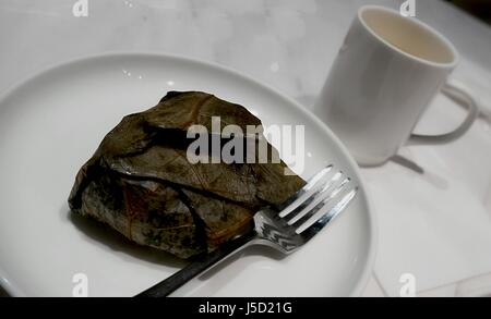 Lo Mai Gai - gewickelt und mit Gabel im Teller serviert und Kaffee Tasse Lo Mai Gai ist Klebreis gefüllt mit Hühnerfleisch, Champignons, Garnelen oder gesalzenem Ei Stockfoto