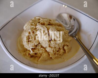 Blick von oben auf eine Schaufel von Schmelzendem Vanilleeis in einer weißen Schüssel mit dem Löffel serviert. Stockfoto