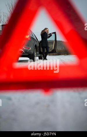 Junge Frau ein Warndreieck Einrichtung und Unterstützung gefordert, nachdem ihr Auto in der Mitte des nirgendwo an einem eiskalten Wintertag ist kaputt Stockfoto