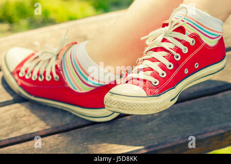 Frau die Füße in einem roten canvas Sneaker mit bunten Socken, sitzen auf einer Bank Stockfoto