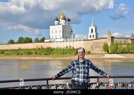 Ein junger Mann steht auf der Aussichtsplattform auf dem Hintergrund der Dreifaltigkeitskathedrale in Pskow Stockfoto