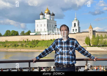 Ein junger Mann steht auf der Aussichtsplattform auf dem Hintergrund der Dreifaltigkeitskathedrale in Pskow Stockfoto