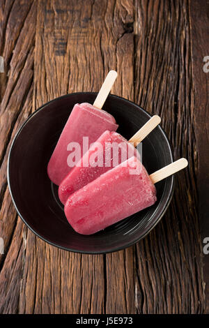 Drei hausgemachte Himbeeren und Vanilleeis erscheint auf einem rustikalen Holz Hintergrund. 3 Berry Eis Eis am Stiel. Sommer essen. Stockfoto