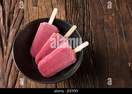 Drei hausgemachte Himbeeren und Vanilleeis erscheint auf einem rustikalen Holz Hintergrund. 3 Berry Eis Eis am Stiel. Sommer essen. Stockfoto