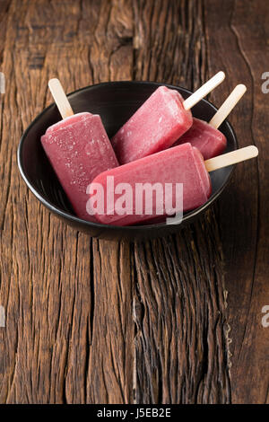 Drei hausgemachte Himbeeren und Vanilleeis erscheint auf einem rustikalen Holz Hintergrund. 3 Berry Eis Eis am Stiel. Sommer essen. Stockfoto