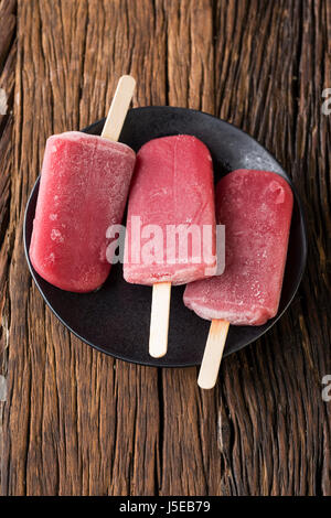 Drei hausgemachte Himbeeren und Vanilleeis erscheint auf einem rustikalen Holz Hintergrund. 3 Berry Eis Eis am Stiel. Sommer essen. Stockfoto