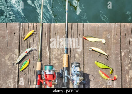 Zwei Angelruten mit Walzen und künstliche Spinnen lockt auf einem hölzernen Pier. Stockfoto