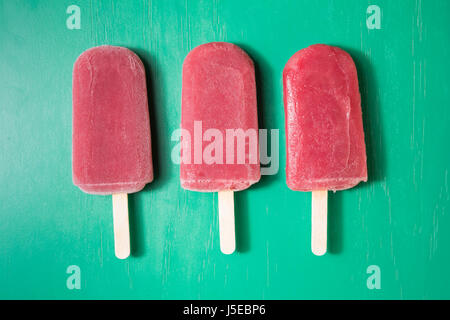 Drei hausgemachte Himbeeren und Vanilleeis erscheint auf grünem Untergrund aus Holz. 3 Erdbeer oder Himbeer Eis Eis am Stiel. Sommer essen. Stockfoto