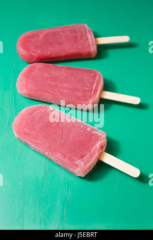 Drei hausgemachte Himbeeren und Vanilleeis erscheint auf grünem Untergrund aus Holz. 3 Erdbeer oder Himbeer Eis Eis am Stiel. Sommer essen. Stockfoto