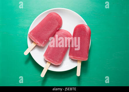 Drei hausgemachte Himbeeren und Vanilleeis erscheint auf grünem Untergrund aus Holz. 3 Erdbeer oder Himbeer Eis Eis am Stiel. Sommer essen. Stockfoto