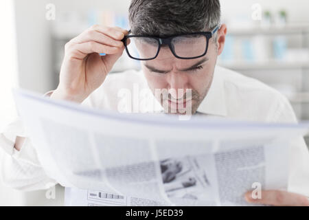 Kaufmann im Büro, schlechte Nachrichten auf einer finanziellen Zeitung lesen ist er schockiert und seine Brille anpassen Stockfoto