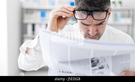 Kaufmann im Büro, schlechte Nachrichten auf einer finanziellen Zeitung lesen ist er schockiert und seine Brille anpassen Stockfoto