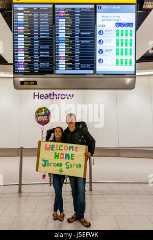 Ein junges Paar hält eine Willkommen Zuhause melden Sie nach seiner Rückkehr von der Reise, Flughafen Heathrow, London, UK Stockfoto