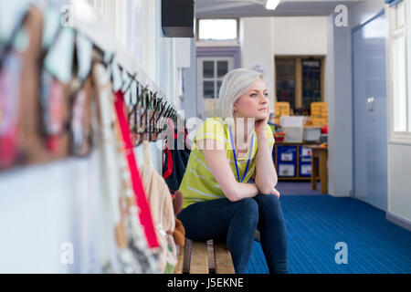 Junge, weibliche Lehrer sitzen auf einer Bank in der Garderobe der Schule. Sie blickt nachdenklich aus dem Fenster. Stockfoto