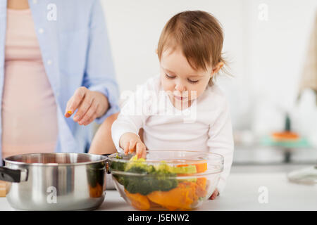 Baby mit Gemüse und Mutter zu Hause kochen Stockfoto