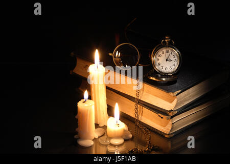 Vintage Taschenuhr und Brille auf alte Bücher in der Nähe von Anzünden von Kerzen Stockfoto