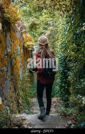 Junge Frau mit blonden Dreadlocks mit Fotokamera beobachten Dschungel. Abenteuer und Reisen. Stockfoto