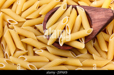 Rohe Penne-Nudeln in den Holzlöffel ist im Vordergrund. Nudeln auf dem Hintergrund Stockfoto