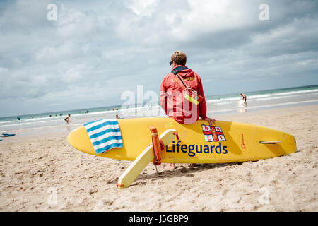 Liam, australischer RNLI-Rettungsschwimmer, sitzt auf seinem Surfbrett und hat ein wachsames Auge über dem Gwihian Beach in Cornwall. Stockfoto