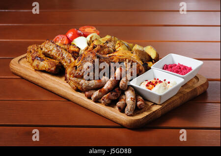 großes Holzbrett mit Rippchen und Steaks gebacken in Senfsauce, Würstchen, gebackene Kartoffel, gegrillte Tomaten und Zwiebel, scharfer Sauce und horseraddis Stockfoto