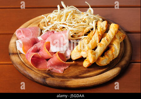 Verschiedene kalte Bier Snacks auf einem runden Holzbrett. Getrockneter Tintenfisch, Prosciutto Crudo und gesalzene Chips Stockfoto