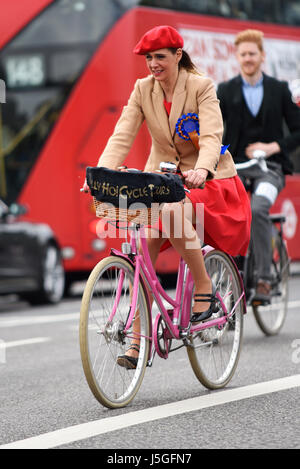 Weibliche Tally Ho Cycle Tours Tweed Run Radfahrerin in London überquert die Westminster Bridge und fährt an einem roten Londoner Bus vorbei Stockfoto