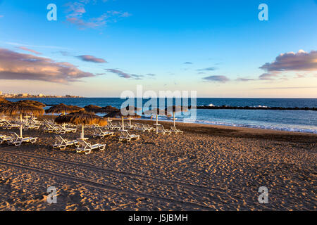 Stroh Sonnenschirme und Liegestühle bei Sonnenuntergang am Playa del Duque in Costa Adeje, Teneriffa, Spanien Stockfoto