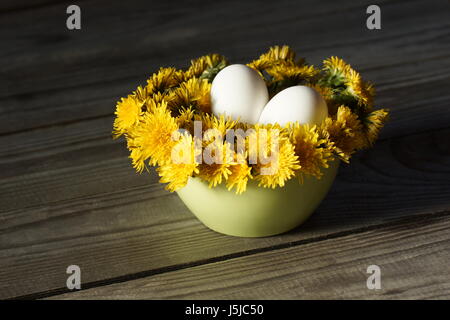 Cute Frühjahr Stillleben. Eiern liegen auf einem Kissen von Löwenzahn in der Küchenschüssel. Stockfoto