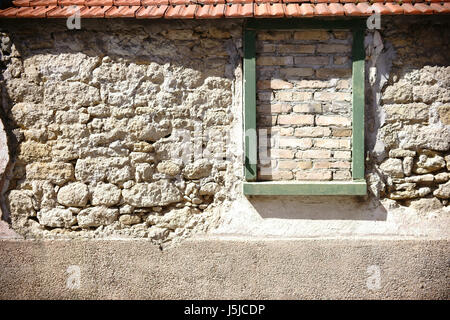 Eine rustikale Wand versetzt und gebrochene Steine mit Dachziegel und einem ummauerten Fensterrahmen. Stockfoto