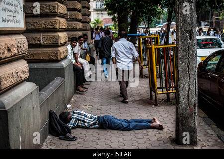 Ein indischer Mann ein Nickerchen mitten auf der Straße während der heißen Stunden in Mumbai, Indien Stockfoto